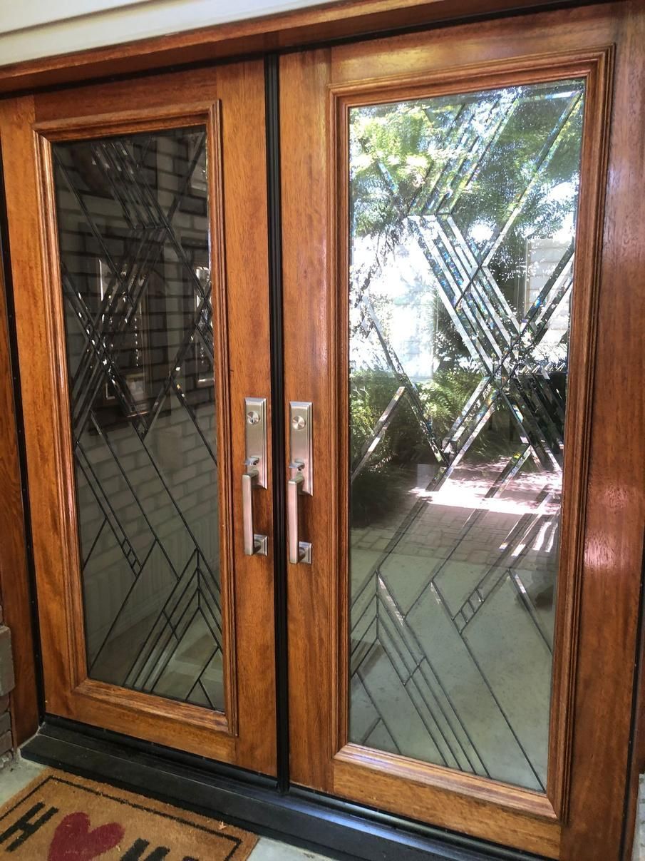 Wooden double doors with glass panels and metal handles, reflecting trees outside.