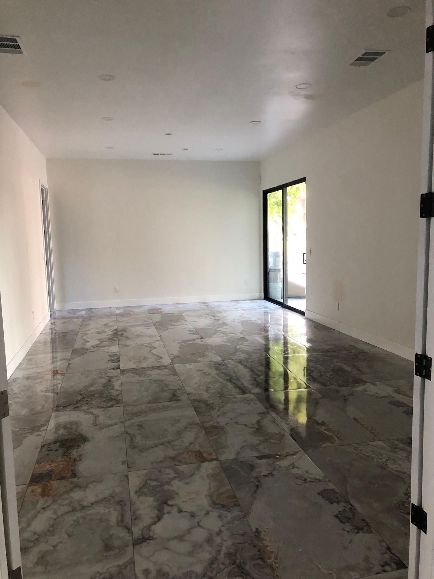 Empty modern room with white walls, glossy marble floor, and glass door letting in daylight