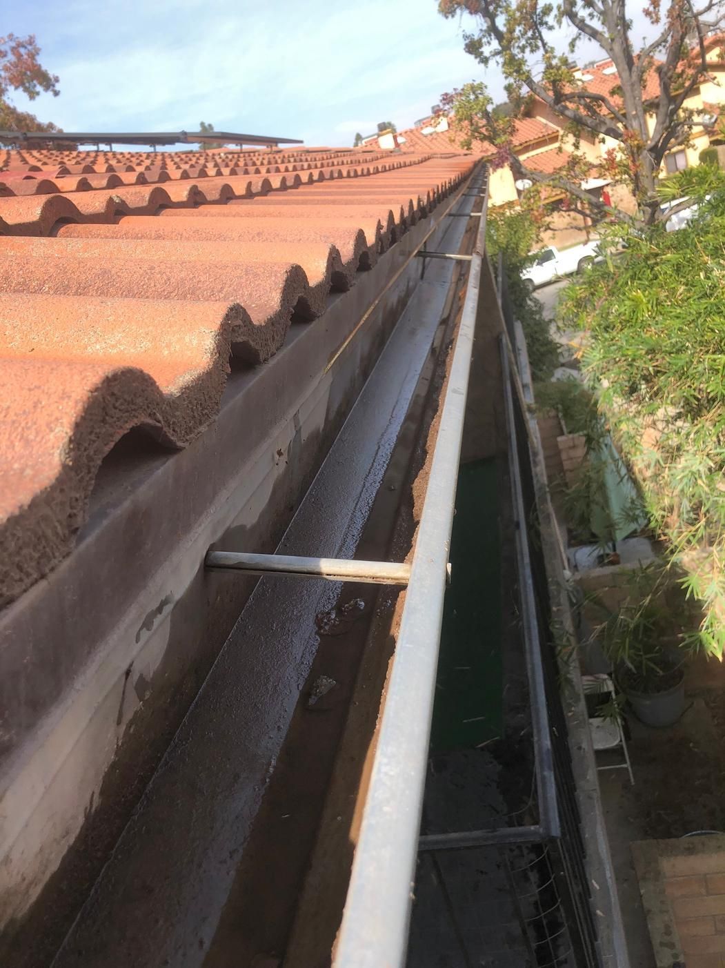 Roof gutter beside red tiled roof and garden, with a narrow water channel in sunlight