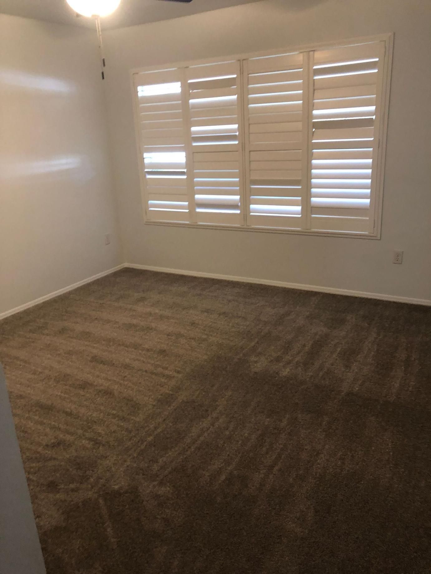 Empty room with brown carpet, white walls, and a window with white plantation shutters.