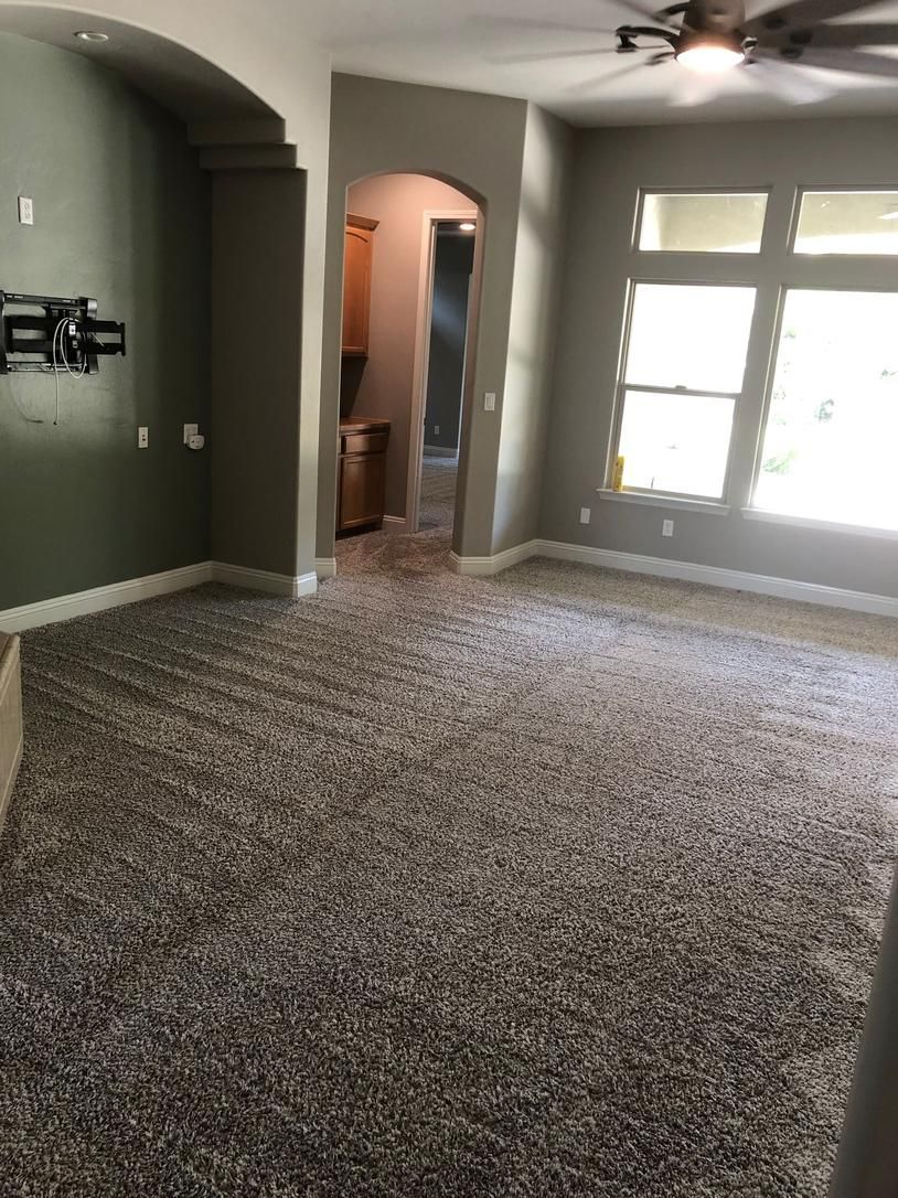 Empty living room with carpeted floor, arched hallway, and bright windows with blinds.