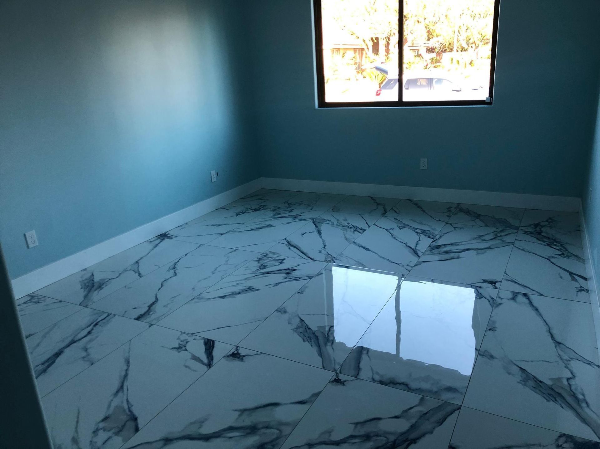 Empty blue room with glossy white marble-pattern floor and a window letting in daylight