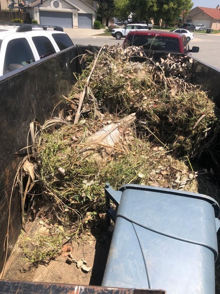 A trailer filled with yard debris and branches, parked in a residential driveway.
