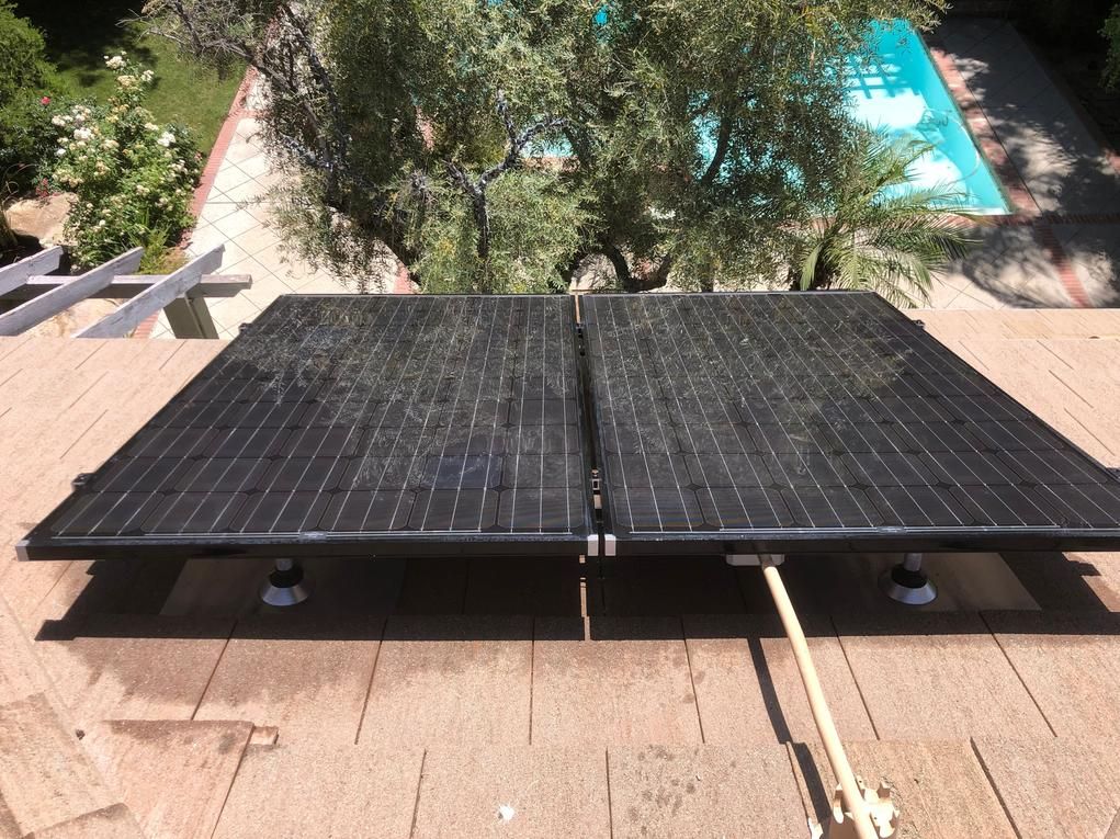 Two black solar panels on a rooftop with trees and a swimming pool in the background