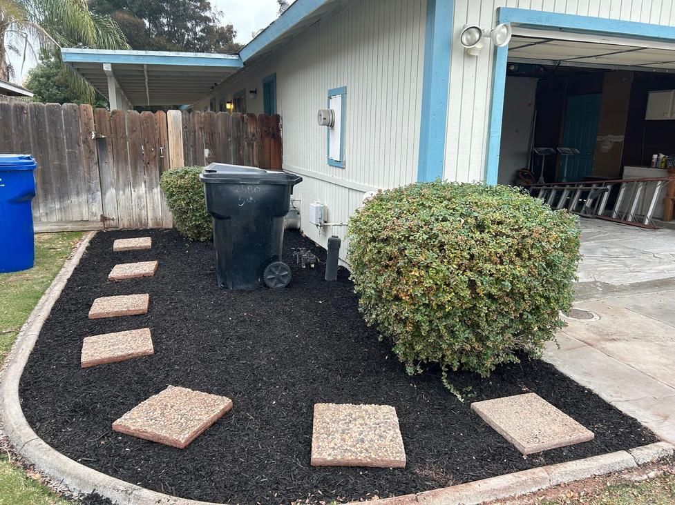 Front yard gravel path with stepping stones, a trash bin, shrub, and an open garage beside a house.