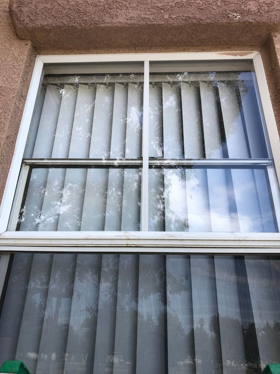 Exterior window with white blinds and a brown stucco wall around it