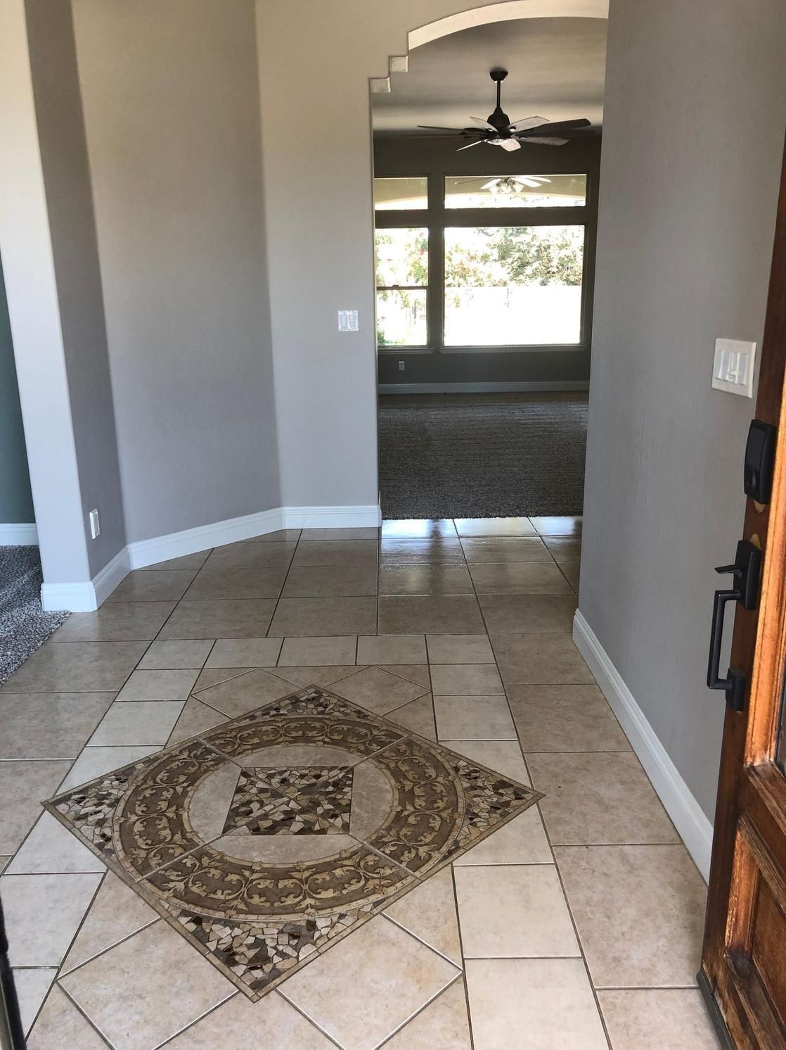 Hallway with tiled floor and decorative center inlay leading to a carpeted room with windows.