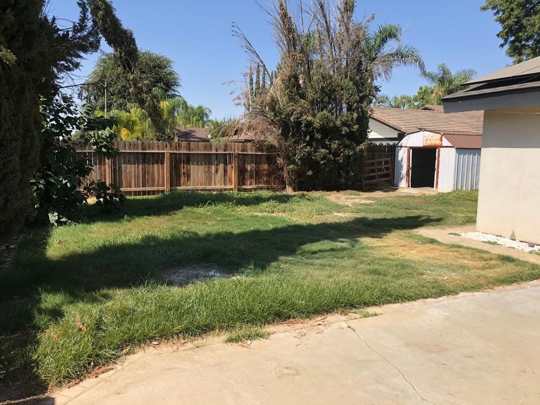 Backyard with grass, wooden fence, trees, and a house with a garage