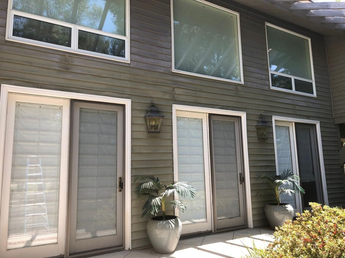 Exterior patio with white French doors, gray siding, potted plant, and upper windows.