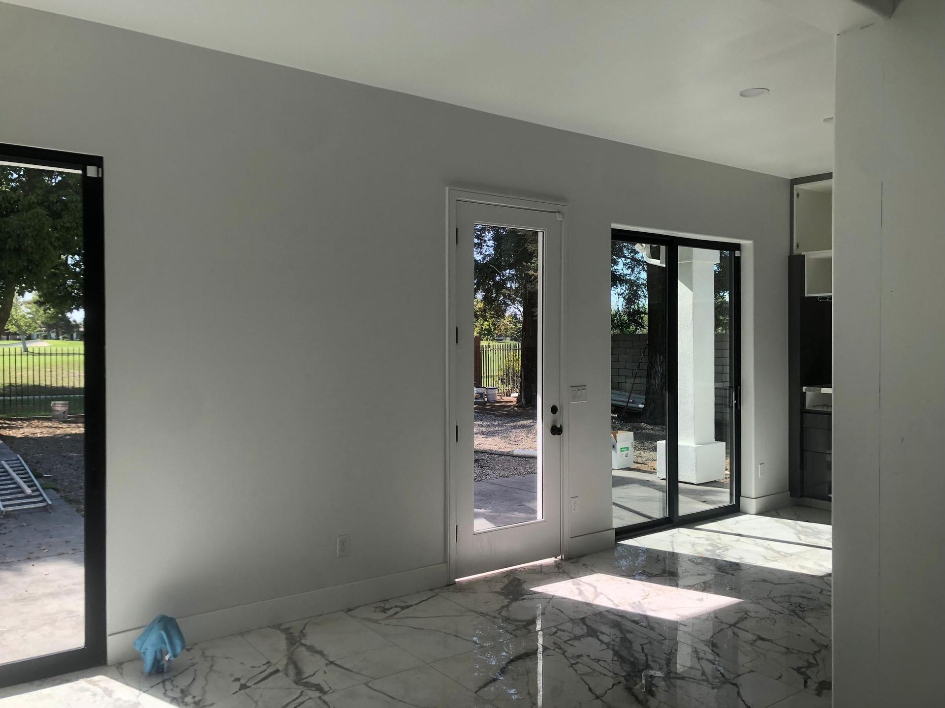 Empty modern room with white walls, cracked tile floor, and glass doors opening to a patio.