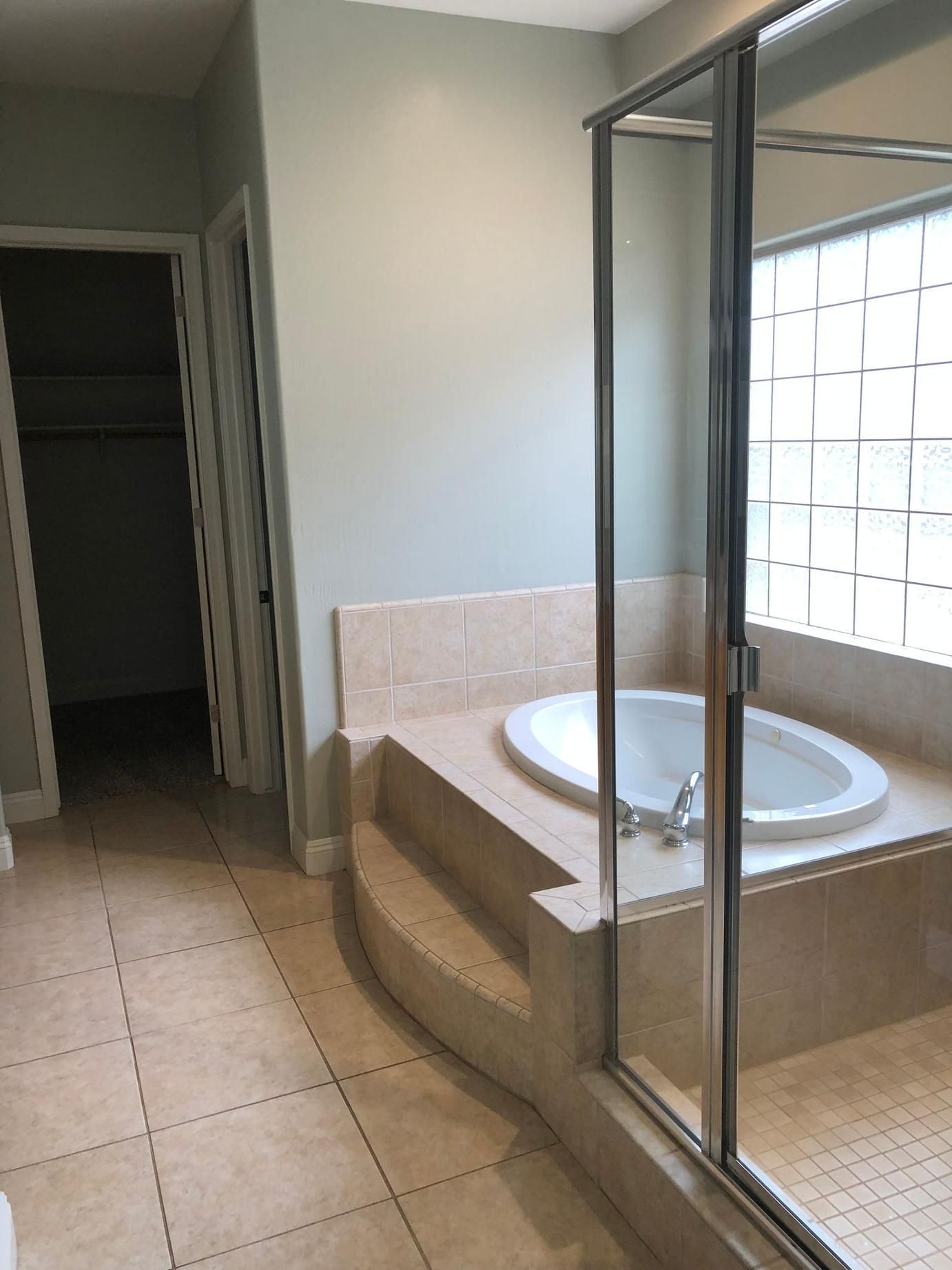 Empty bathroom with beige tile, built-in tub, and glass-enclosed shower.