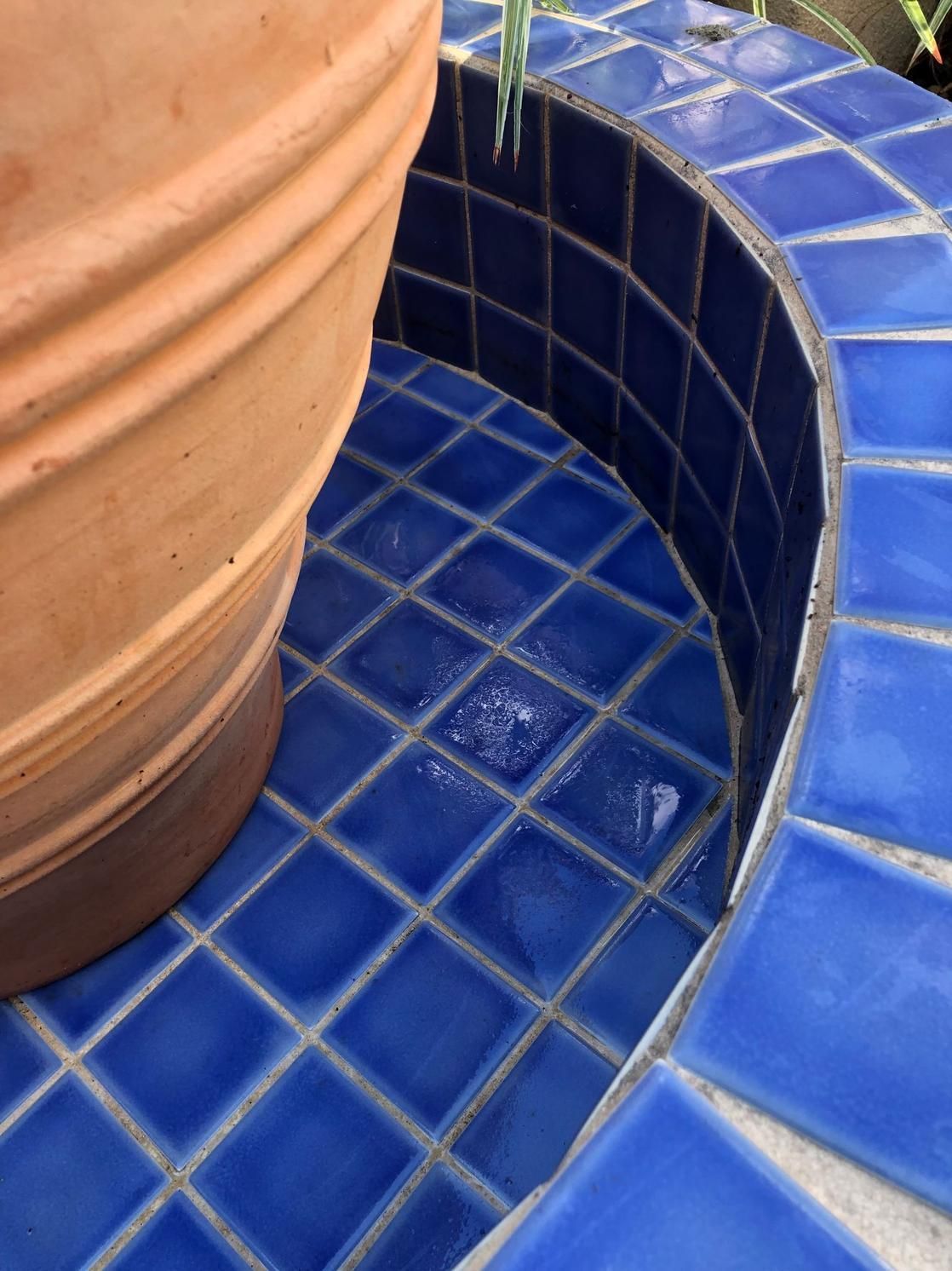 Blue tiled fountain base with a terracotta pot and curved bench edge