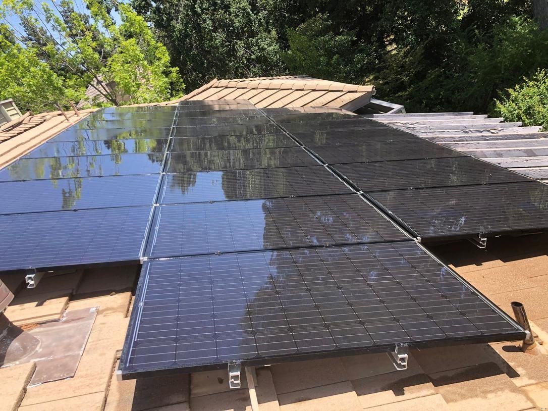 Solar panels installed on a rooftop, reflecting trees and sky.