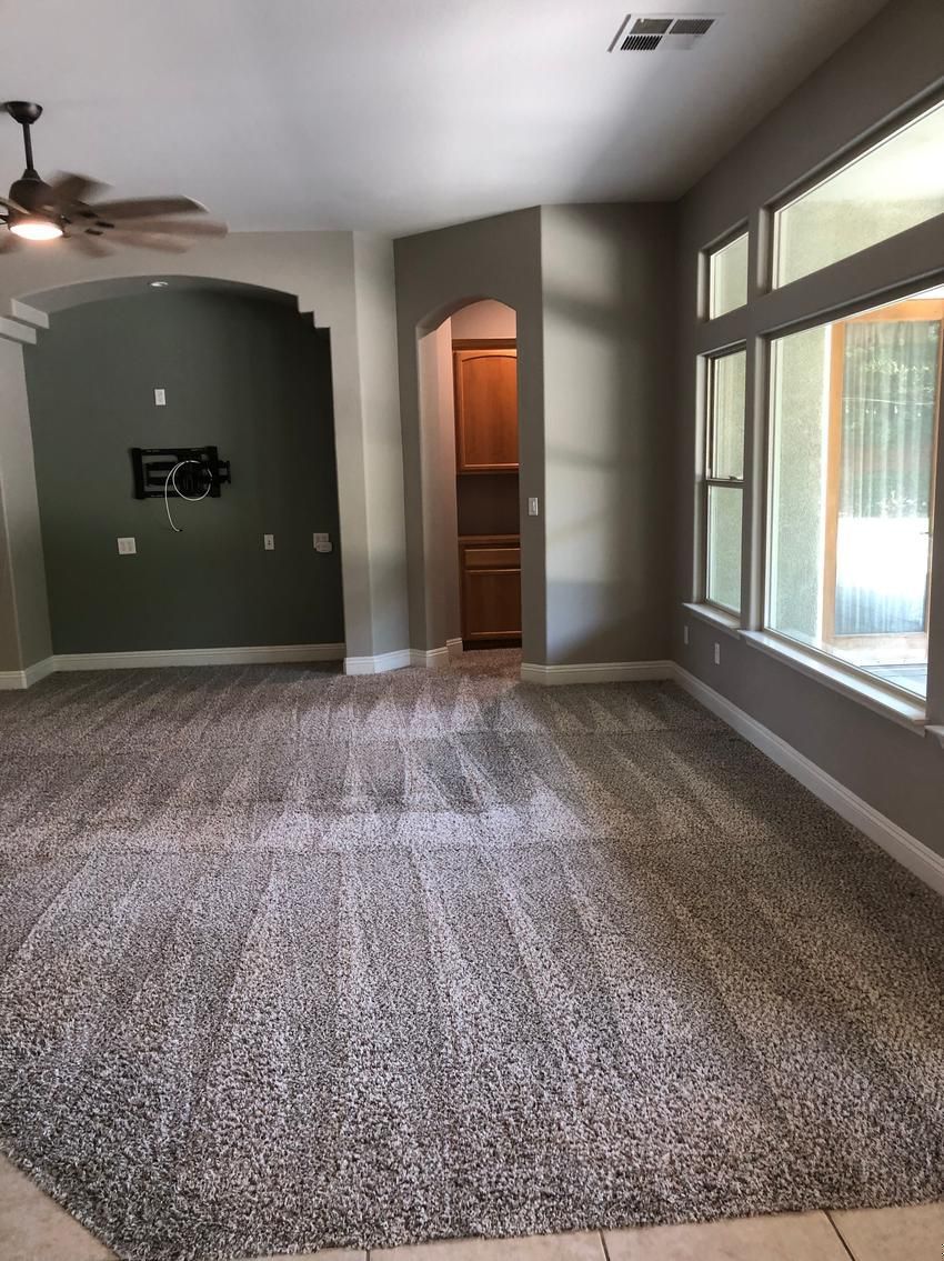 Empty living room with gray walls, carpet, ceiling fan, and large windows on the right.