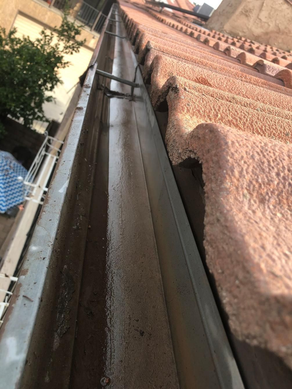 Narrow water slide chute beside a building, viewed from above with trees on the left and brick wall on the right