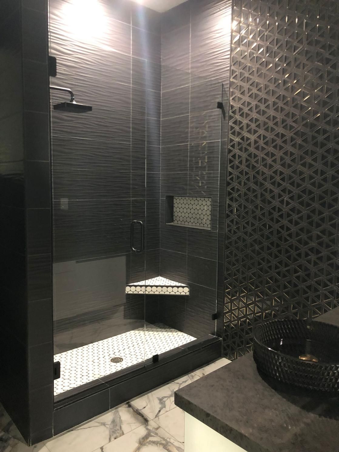 Modern shower with black tiled walls, glass enclosure, and white hexagonal floor tiles.