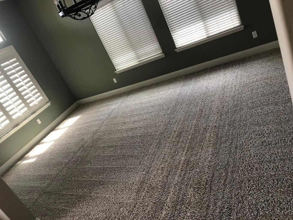 Empty carpeted room with gray walls, white shuttered windows, and ceiling lights.