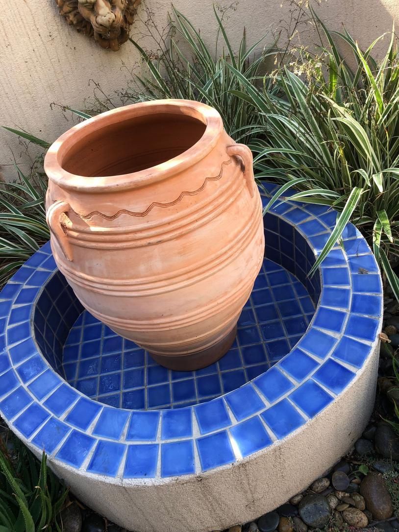Terracotta pot in a blue tiled fountain basin against a stone wall