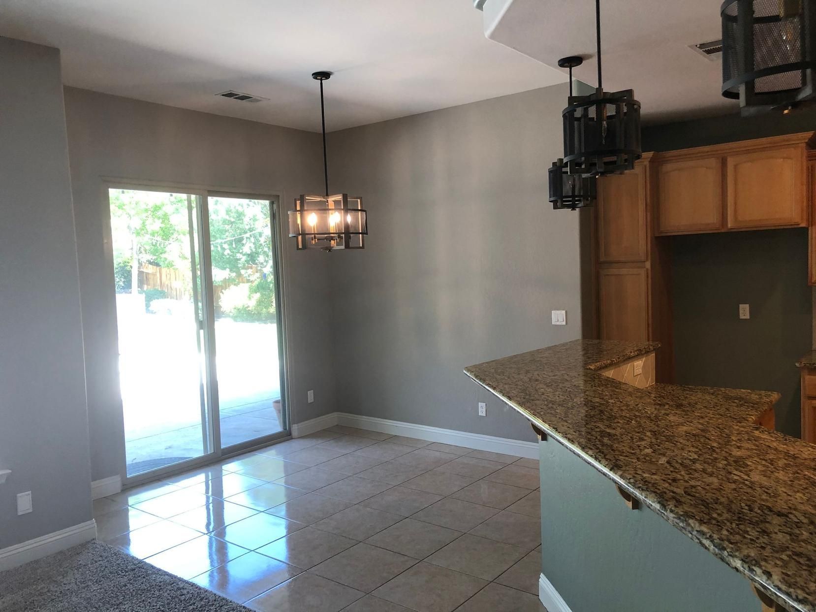 Empty modern kitchen and dining area with tile floor, granite counter, and sliding glass doors.