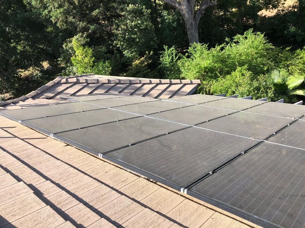Solar panels installed on a roof beside trees and greenery.