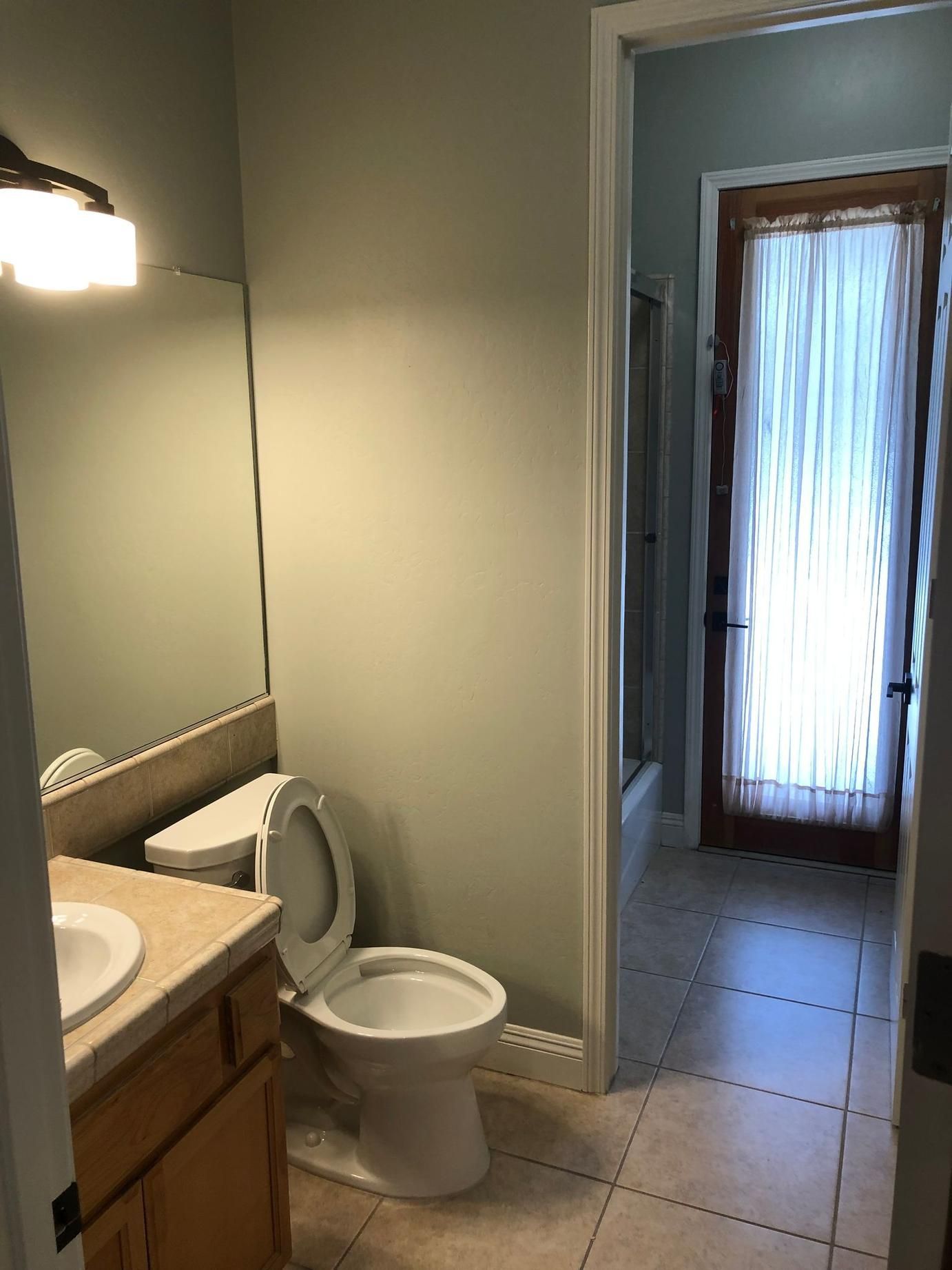 Small bathroom with a toilet, sink, mirror, and open door to a tiled hallway.