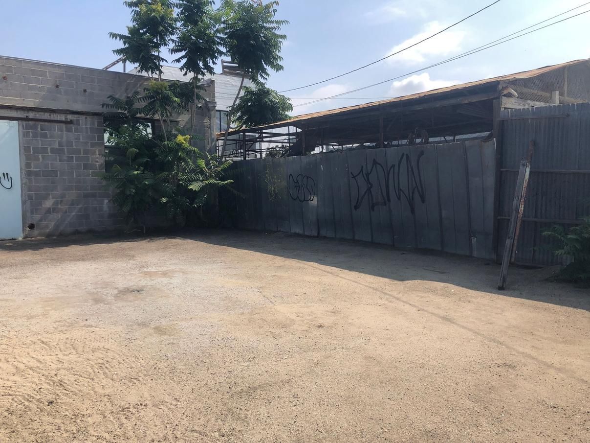 Empty dirt courtyard beside a corrugated metal gate and concrete wall under bright sun