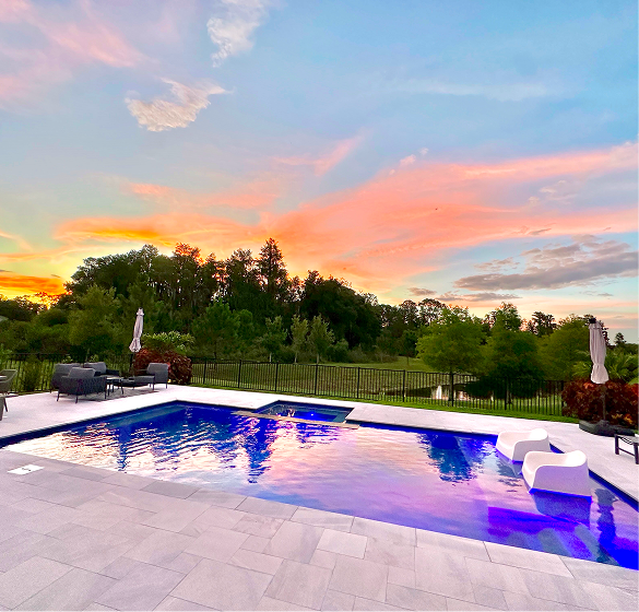 A rectangular pool with turquoise water, a connected spa, and a house in the background. Sunny day.