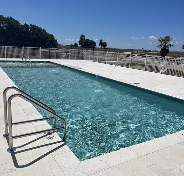 Rectangular swimming pool with clear water, surrounded by white decking and fence, under a blue sky.
