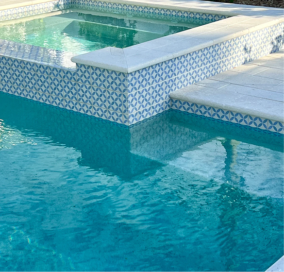 Pool with turquoise water, patterned blue and white tile, and white coping stones.