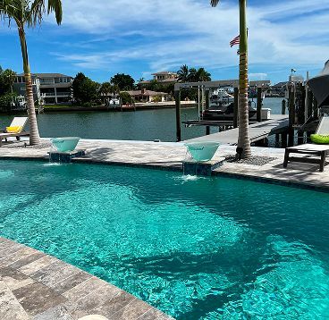 Pool with turquoise water, overlooking a canal, with palm trees and a sunny blue sky.