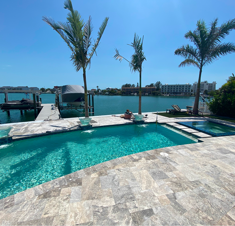 Poolside view with turquoise water, dock, palms, and a person sunbathing.