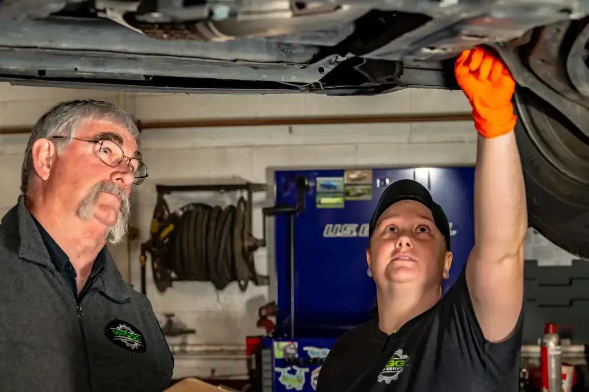 A man and a woman are working under a car in a garage.