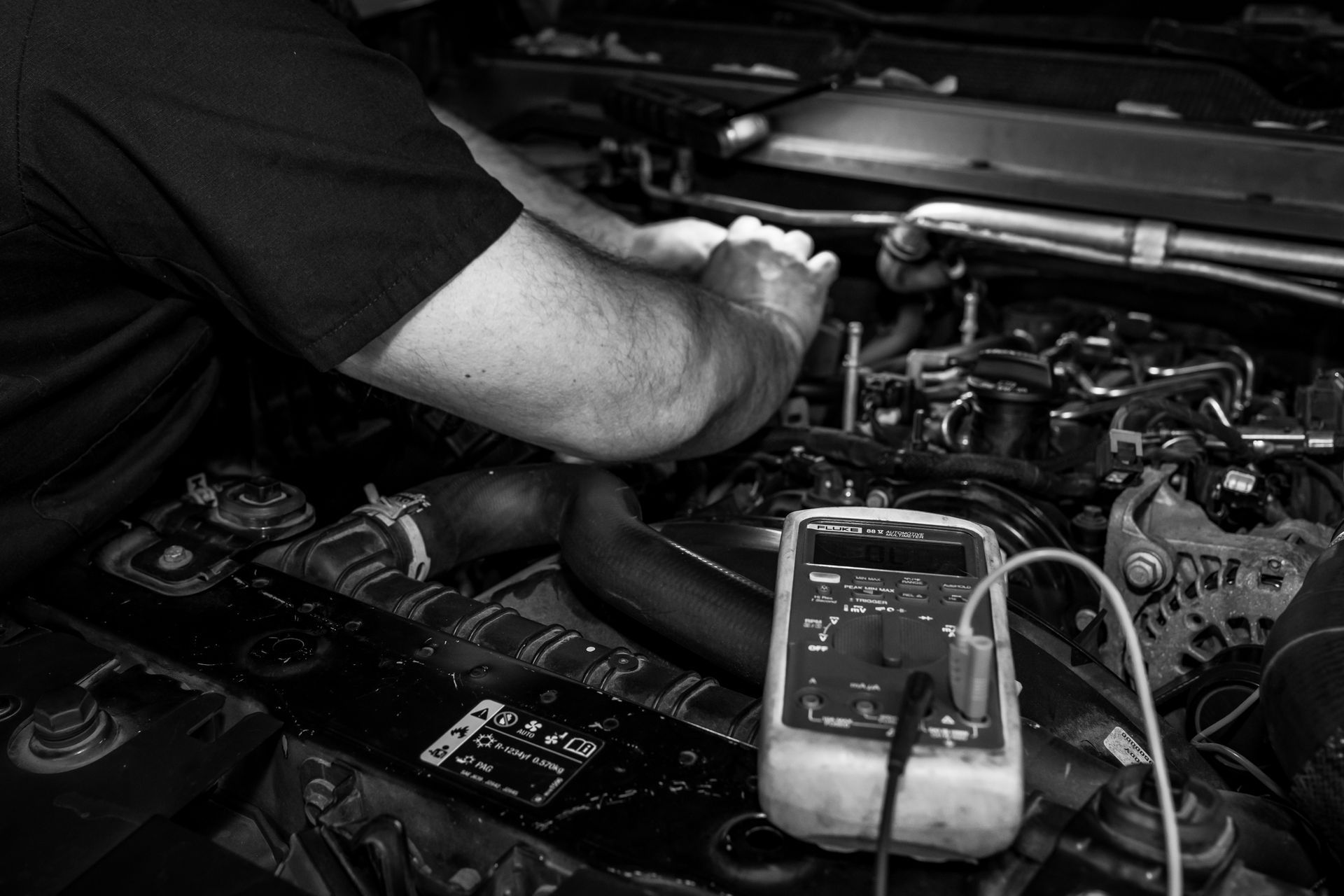 A black and white photo of a man working on a car engine.