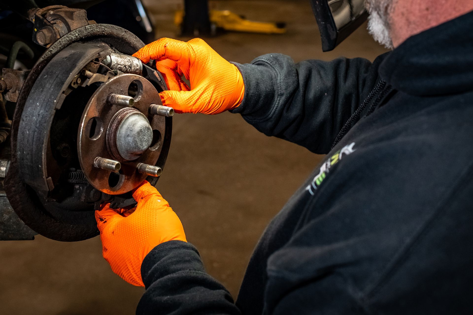A man wearing orange gloves is working on a car wheel.