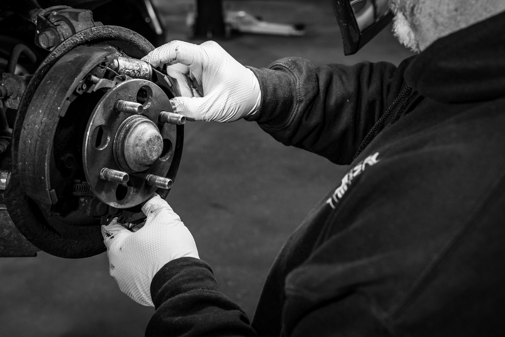 A black and white photo of a man working on a car brake.