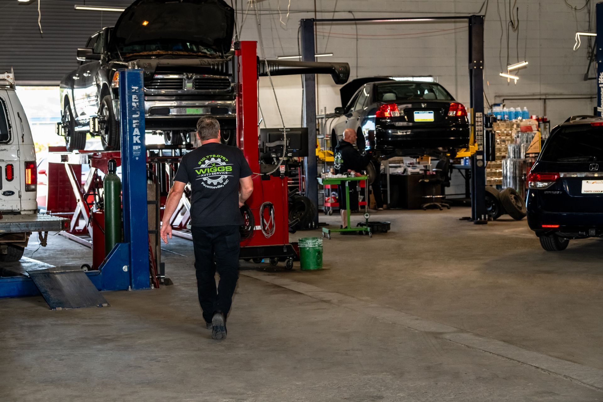 A man is walking through a garage with cars on lifts.