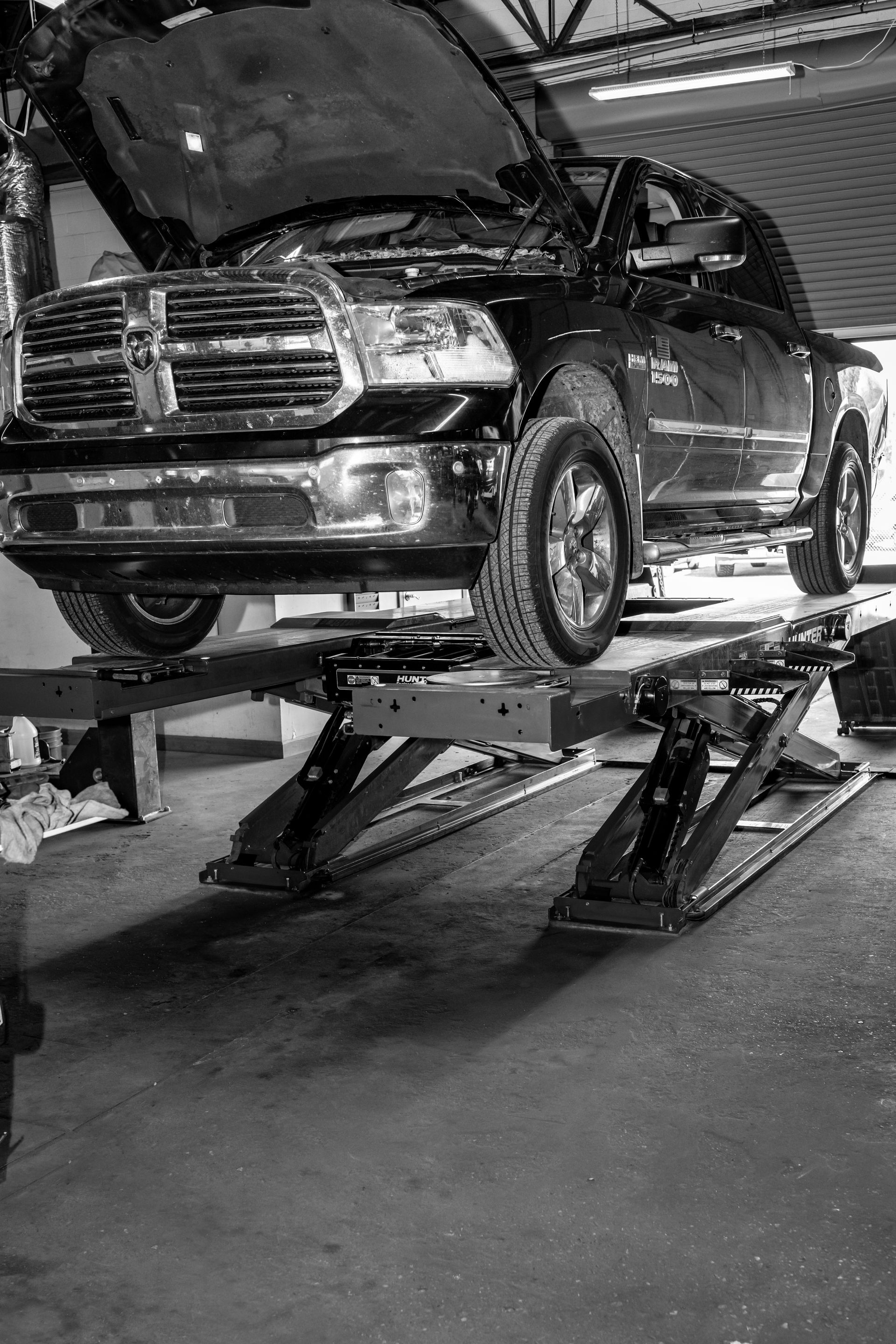 A black and white photo of a truck on a lift in a garage.