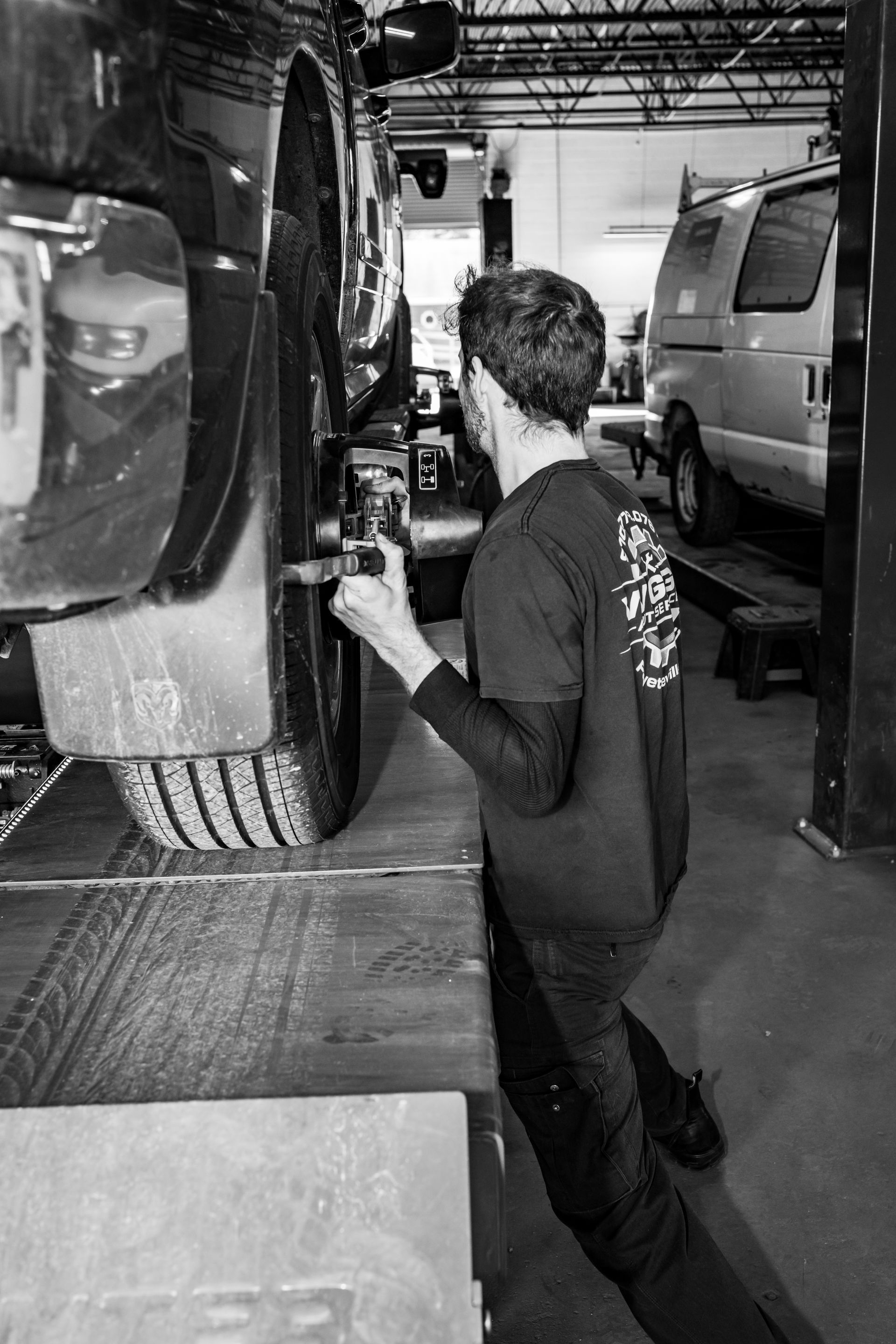 A black and white photo of a man working on a car in a garage.