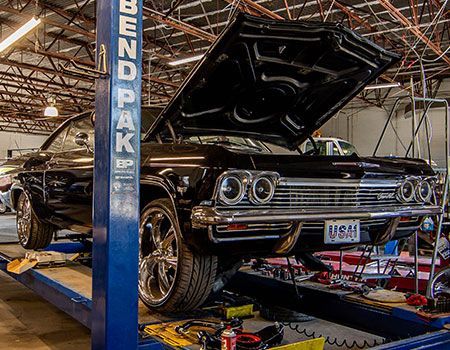 A black car is on a lift in a garage with the hood up.