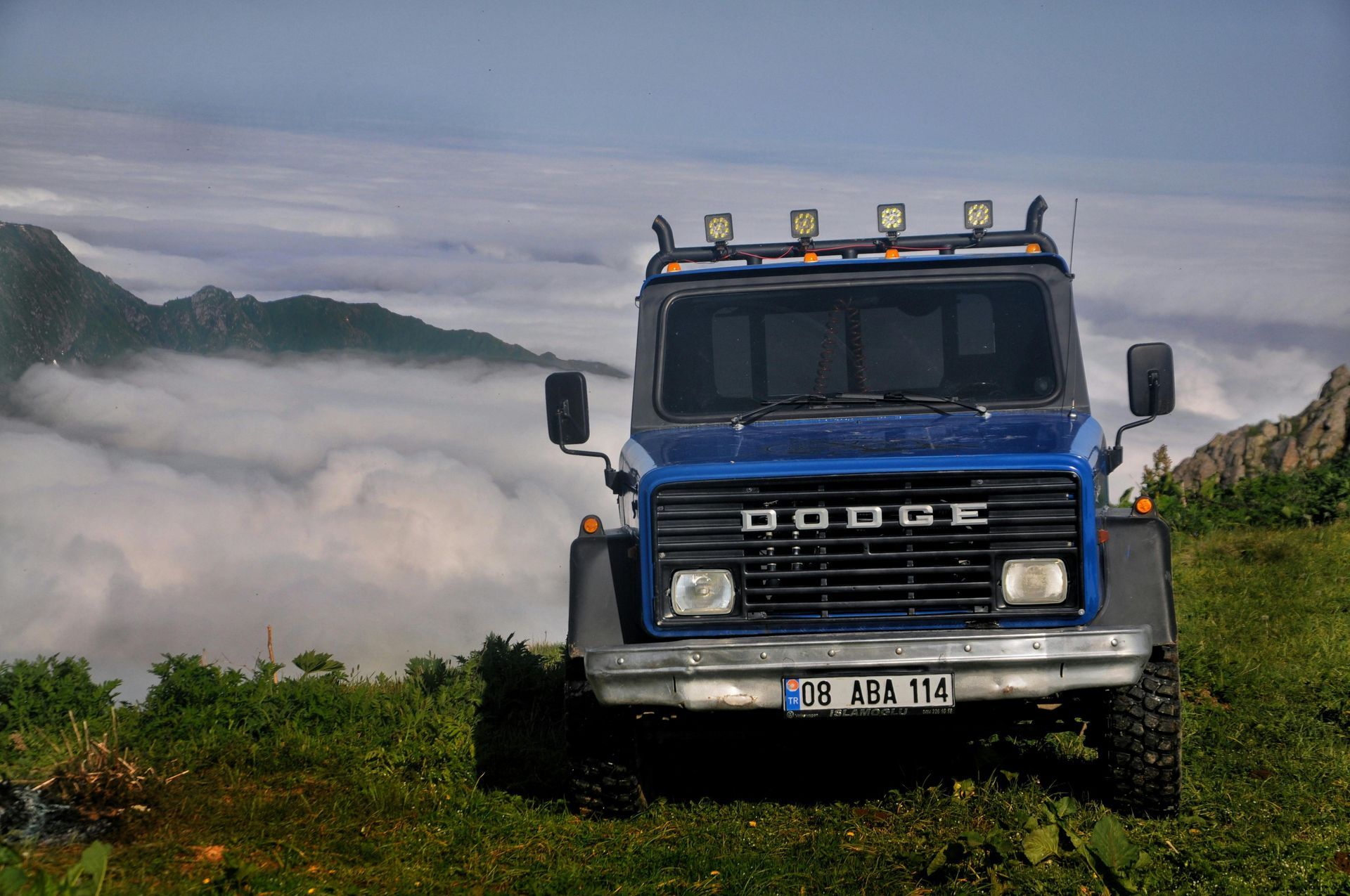 Blue DAF truck driving on a grassy road with misty hills in the background