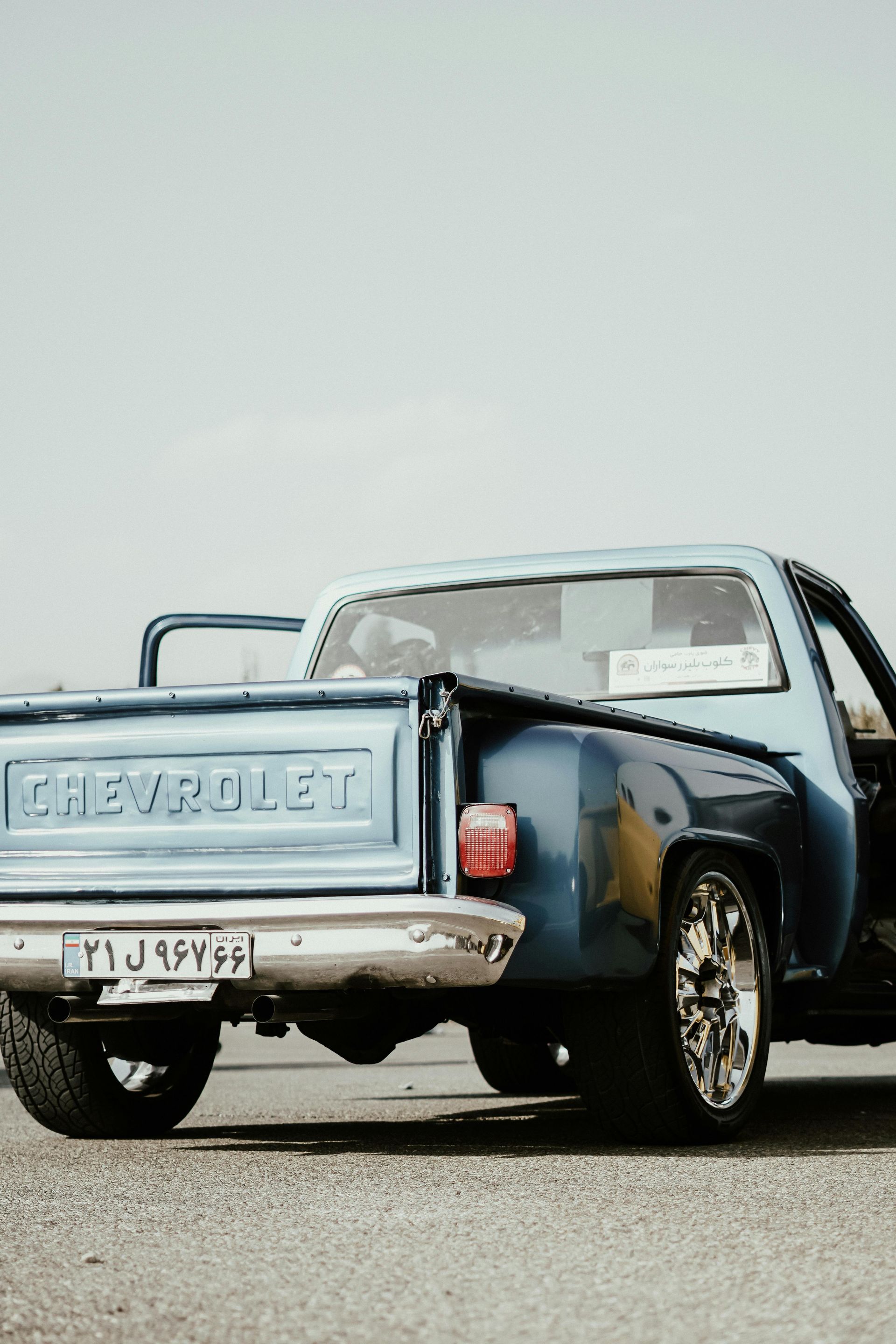 Blue Chevrolet pickup truck parked on a road, rear view with tailgate open and chrome wheels