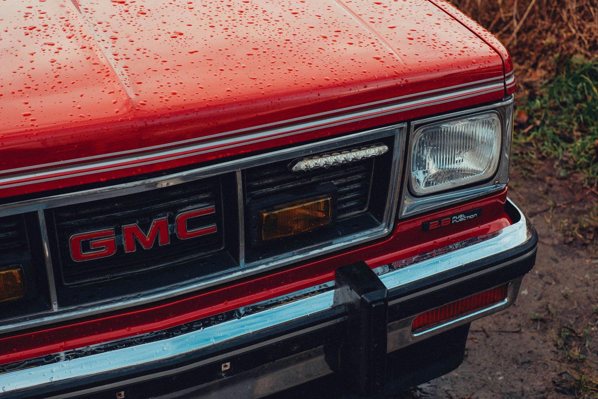 Close-up of a red GMC truck front grille and headlight on a wet road