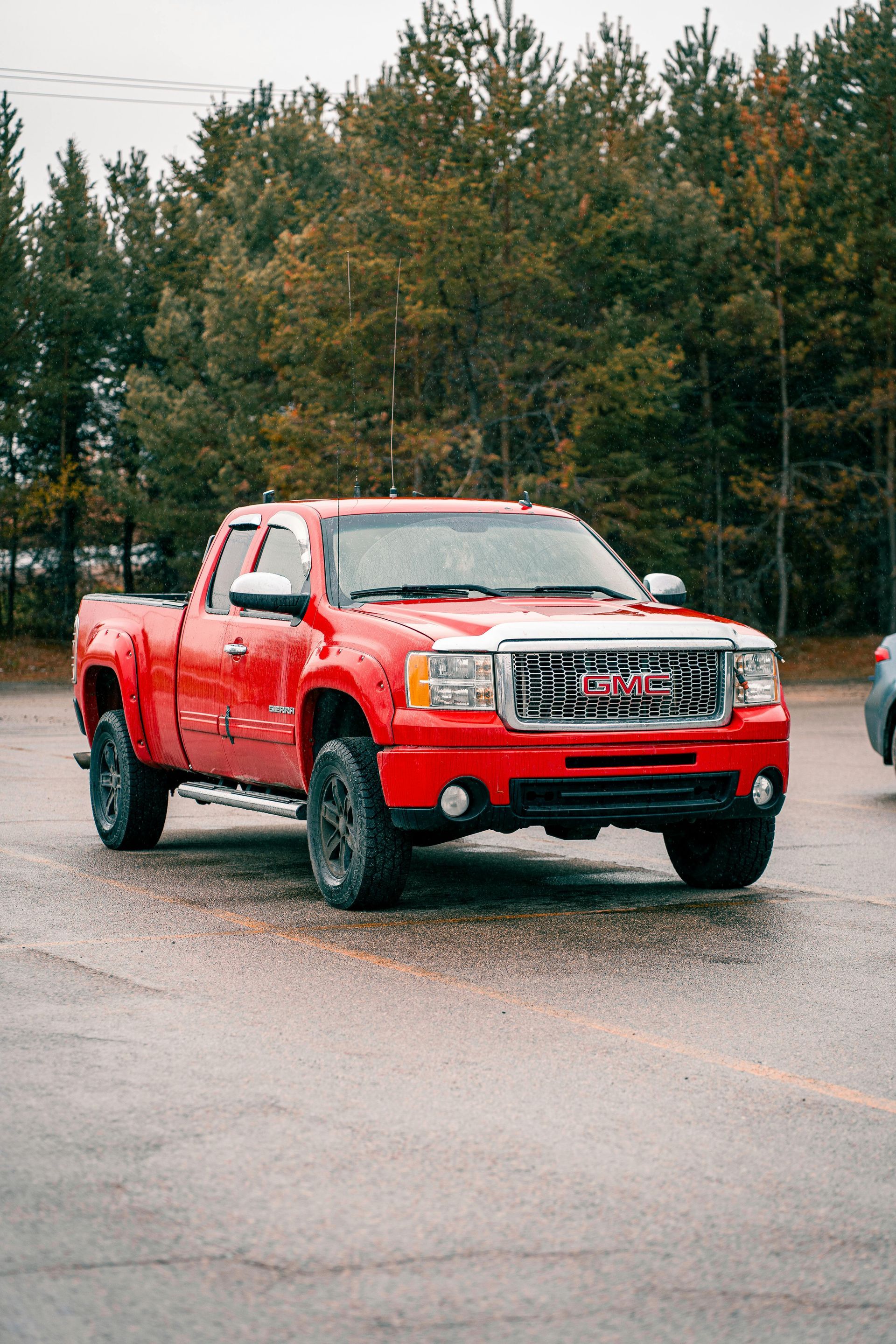 Red GMC pickup truck parked on a wet lot with trees in the background