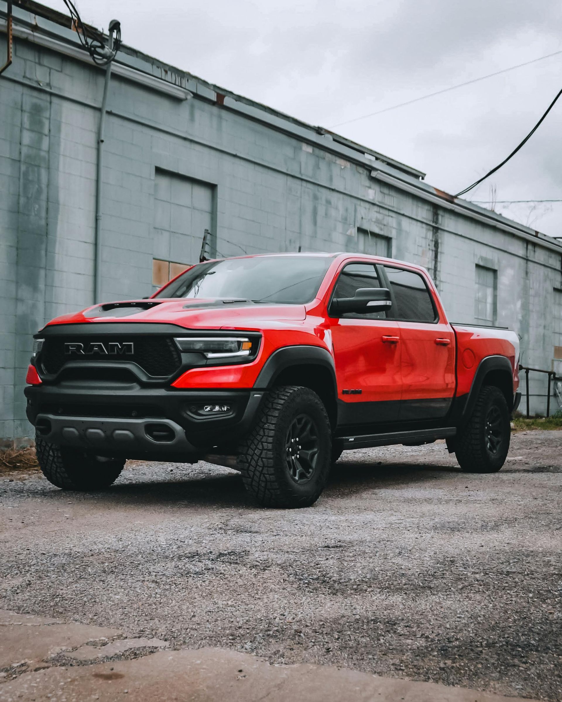 Red off-road pickup truck parked on gravel beside a gray industrial building