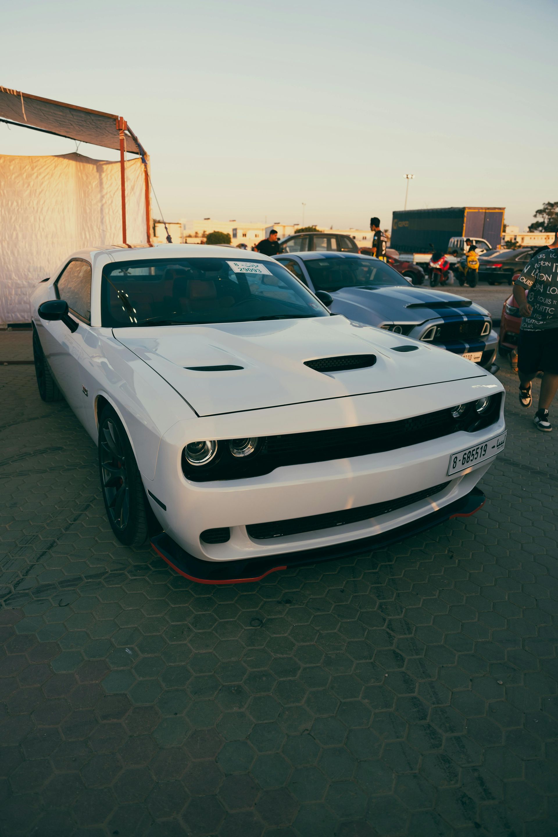 White Dodge Challenger parked outdoors at sunset, with another car and people in the background