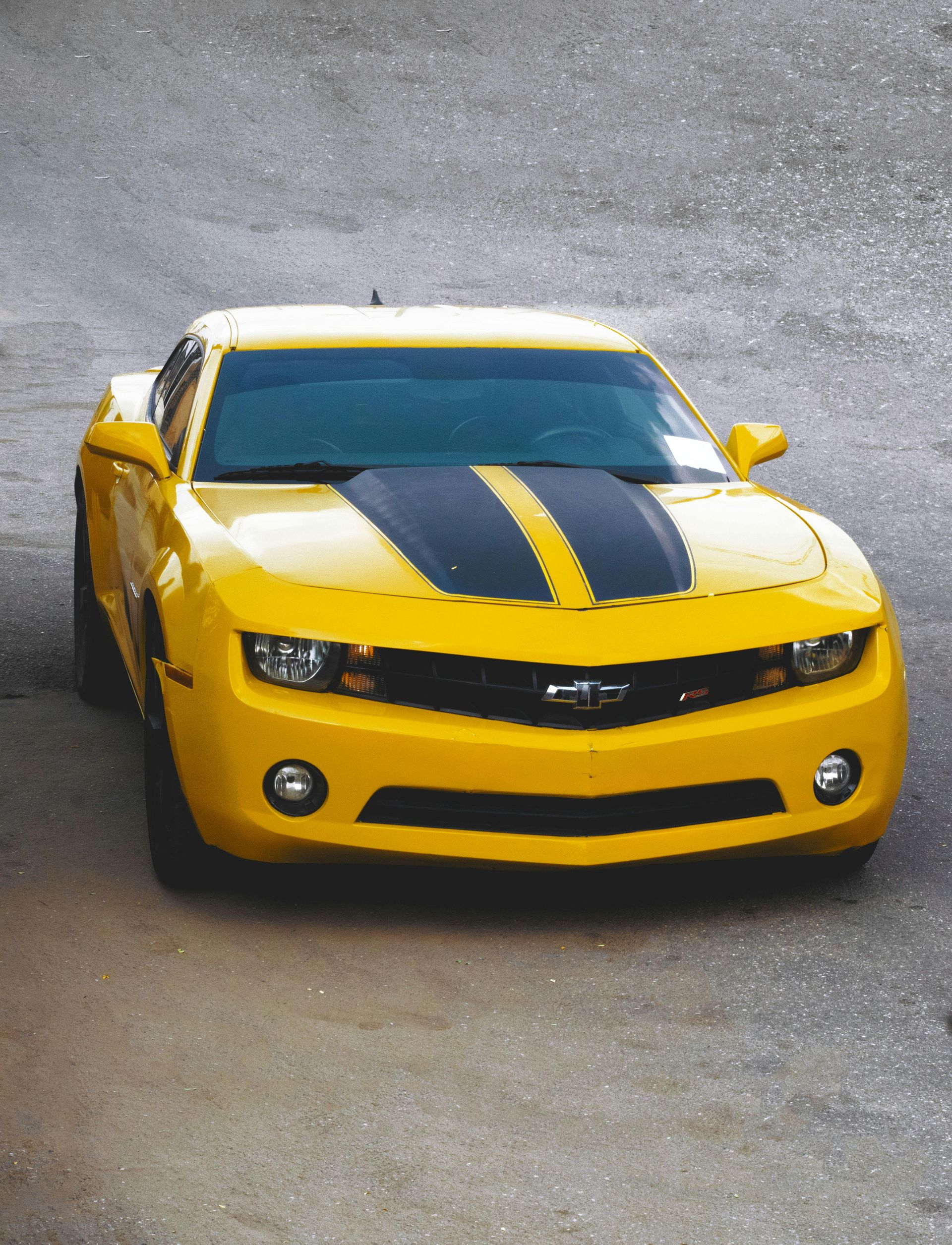 Yellow sports car with black racing stripes parked on a wet road