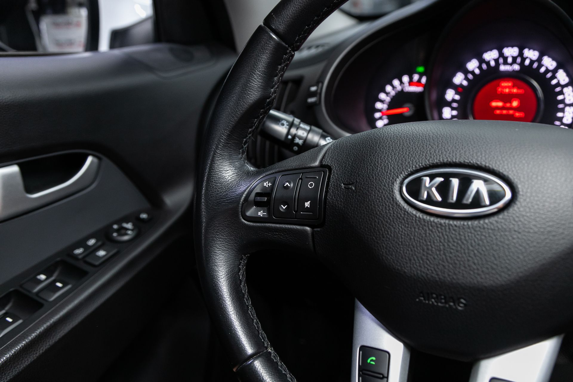 Kia steering wheel and dashboard illuminated at night, with driver’s door controls visible