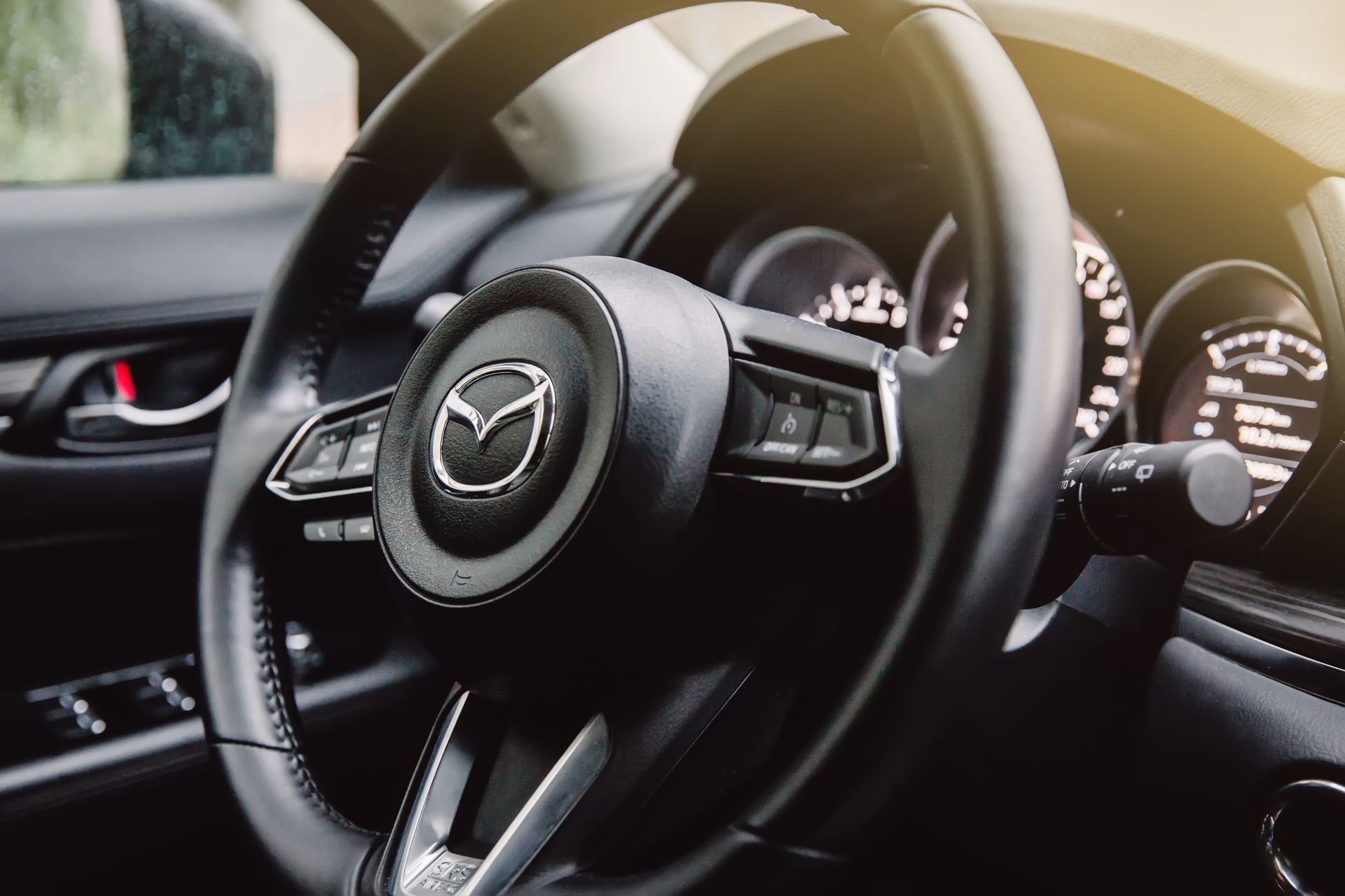 Mazda car interior with steering wheel and dashboard close-up, black leather and silver accents