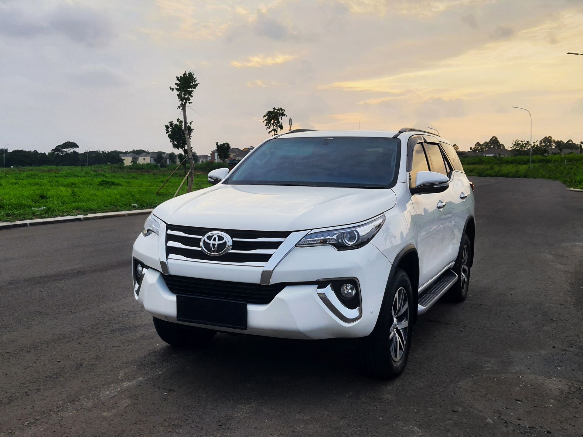 White SUV parked on a road at sunset with green fields and trees in the background