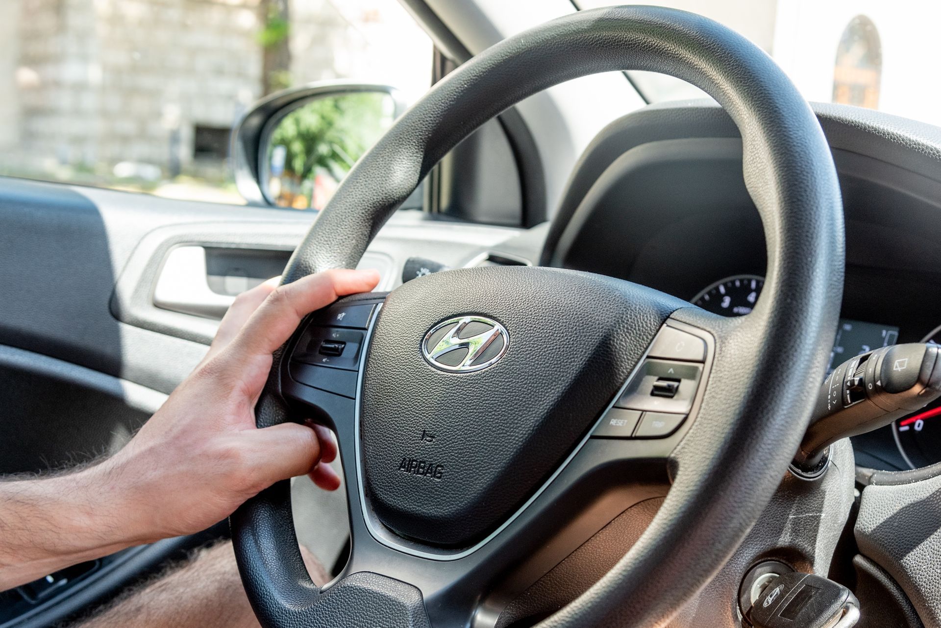 Hand on a car steering wheel, driving on a sunny street